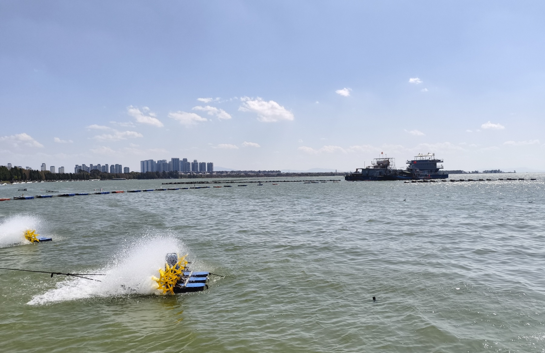Dianchi Lake with water aerators in the foreground, a boat and the Kunming shoreline beyond.